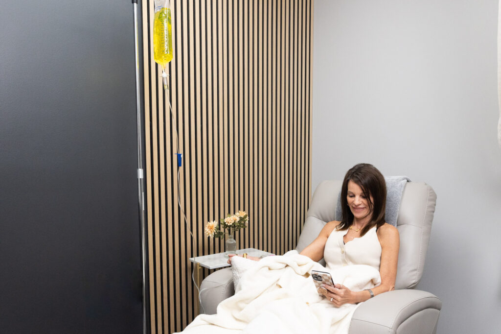 A brunette woman sitting comfortably in one of the treatment chairs at Clarity Health & Aesthetics while she receives one of the many IV therapies in Kansas City.